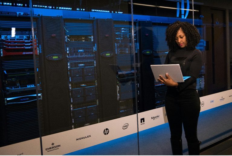A worker examines a laptop screen in front of a datacenter storage terminal.