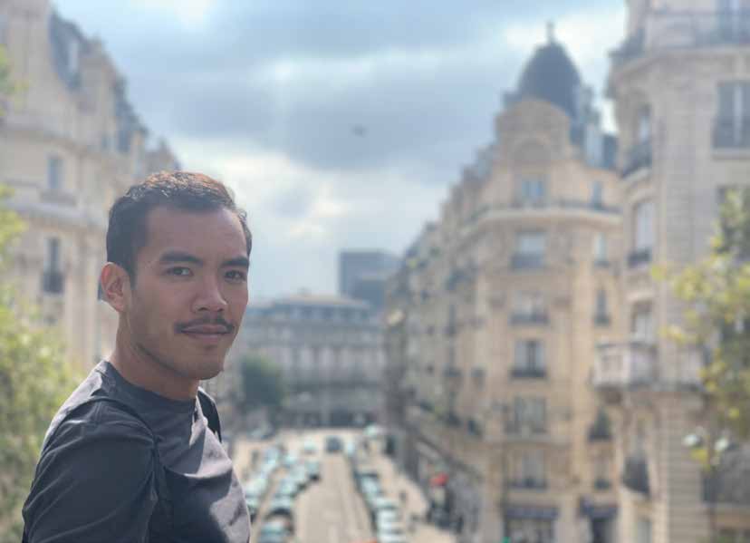 A headshot of joshua son standing in front of buildings