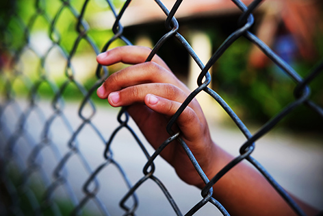 Hand of a young offender against a chain-link fence.