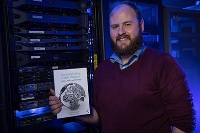 Christopher Whyte,Ph.D., an assistant professor at the VCU Wilder School, displays his latest book, “Understanding Cyber Warfare: Politics, Policy and Strategy.”
